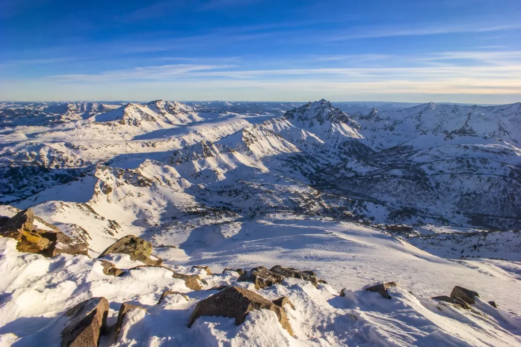 View from the summit of Red Lodge Mountain looking south toward the Beartooth Plateau and the closed Beartooth Highway with vast snow-covered peaks stretching to the horizon