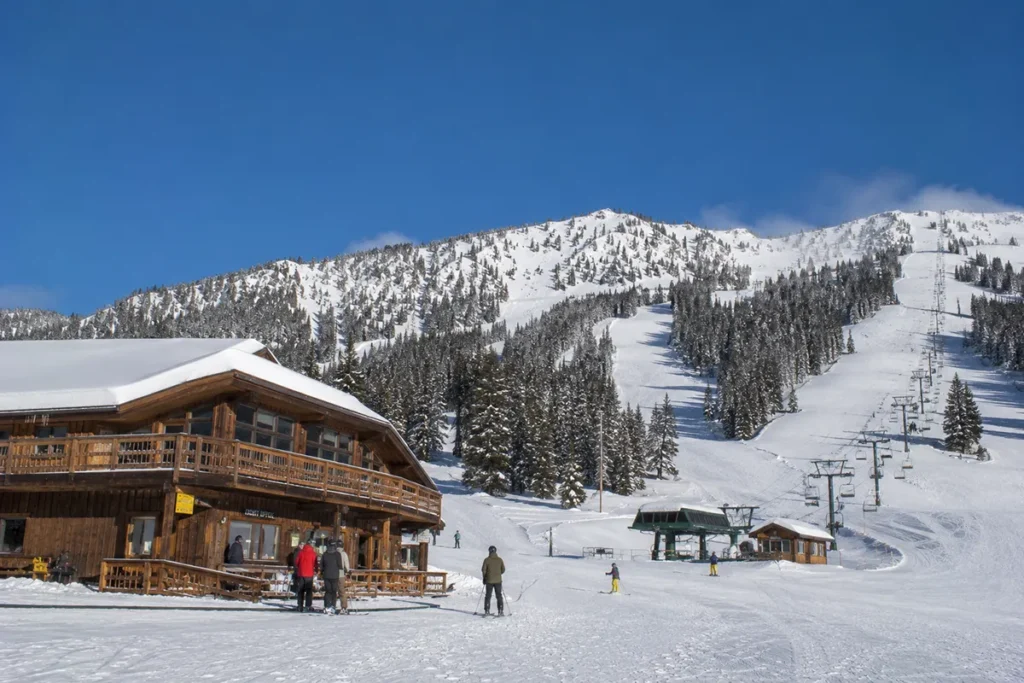 Wide view of Lookout Pass Ski Area with the historic lodge in the foreground and the Eagle Peak expansion terrain rising in the background under a clear blue sky