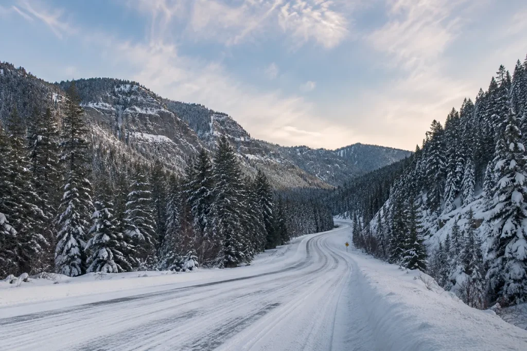 Snow-covered US Highway 89 winding through the Little Belt Mountains with dense conifer forest on both sides and a Kings Hill Pass elevation sign visible