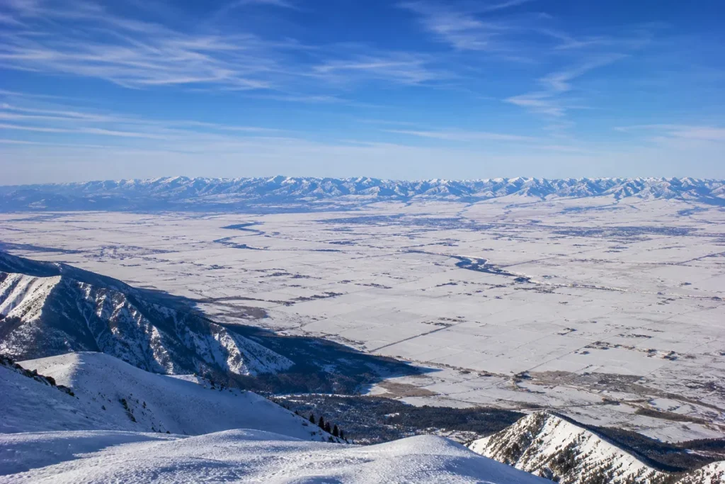 Wide view from the top of the Bridger lift looking down the east-facing slopes of Bridger Bowl across the Gallatin Valley with the Spanish Peaks visible in the distance