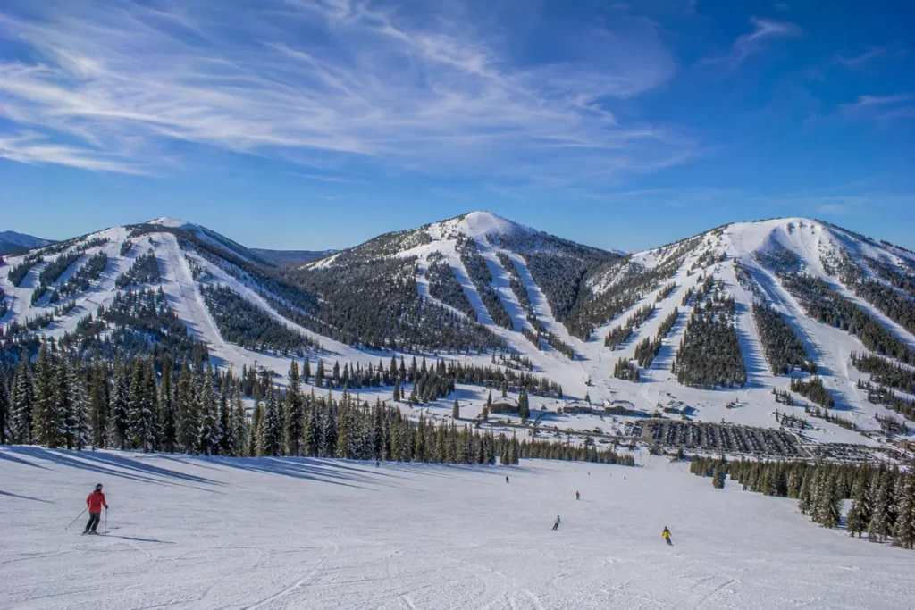 Wide view of Great Divide Ski Area with multiple ski runs visible across three mountain peaks under bright Montana sunshine on a clear winter day
