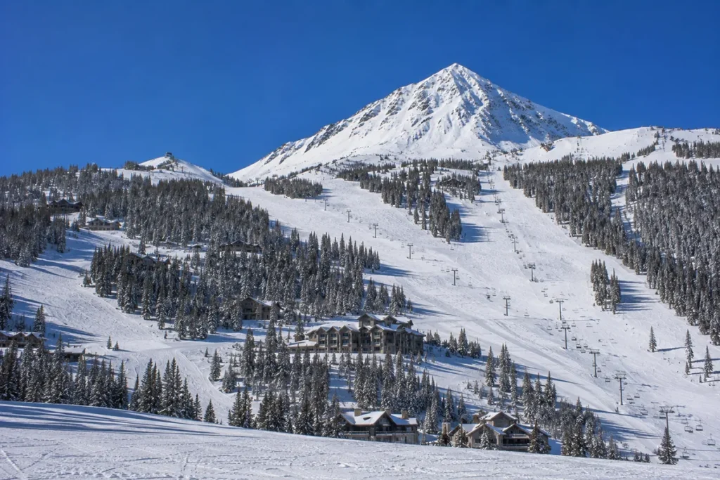 View of Pioneer Mountain rising above the snow-covered Yellowstone Club terrain with chairlifts visible and private residential lodges scattered through the landscape