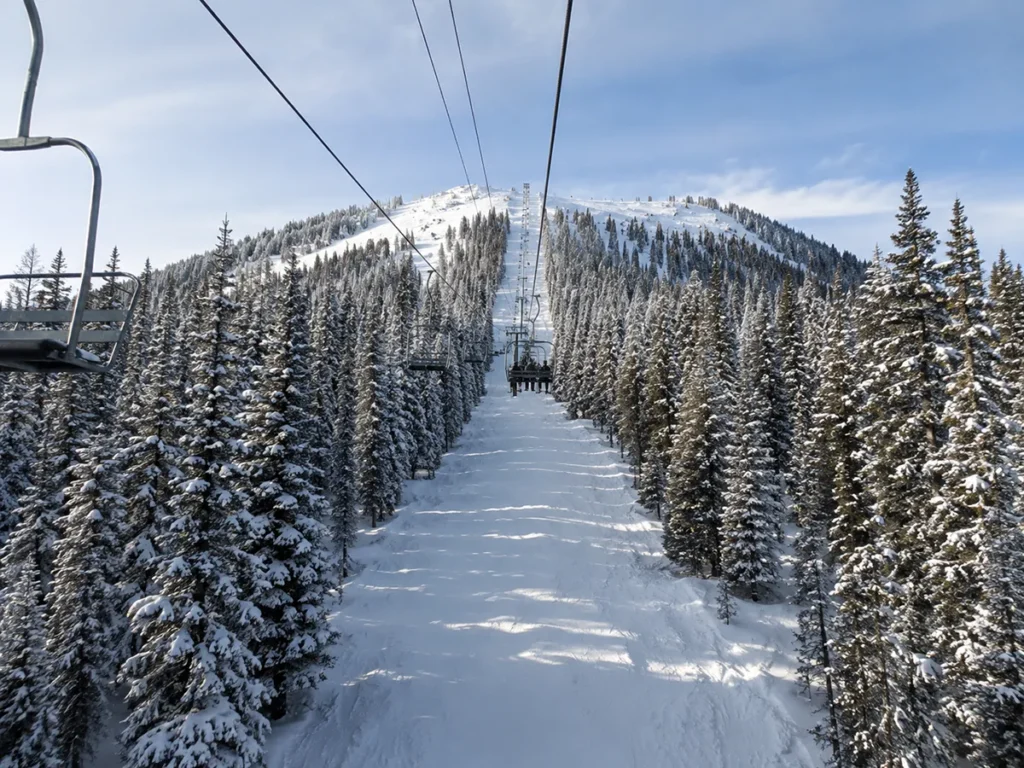 A skier on the Prospector triple chair at Showdown Montana riding up through snow-covered evergreen trees with the summit ridge visible above