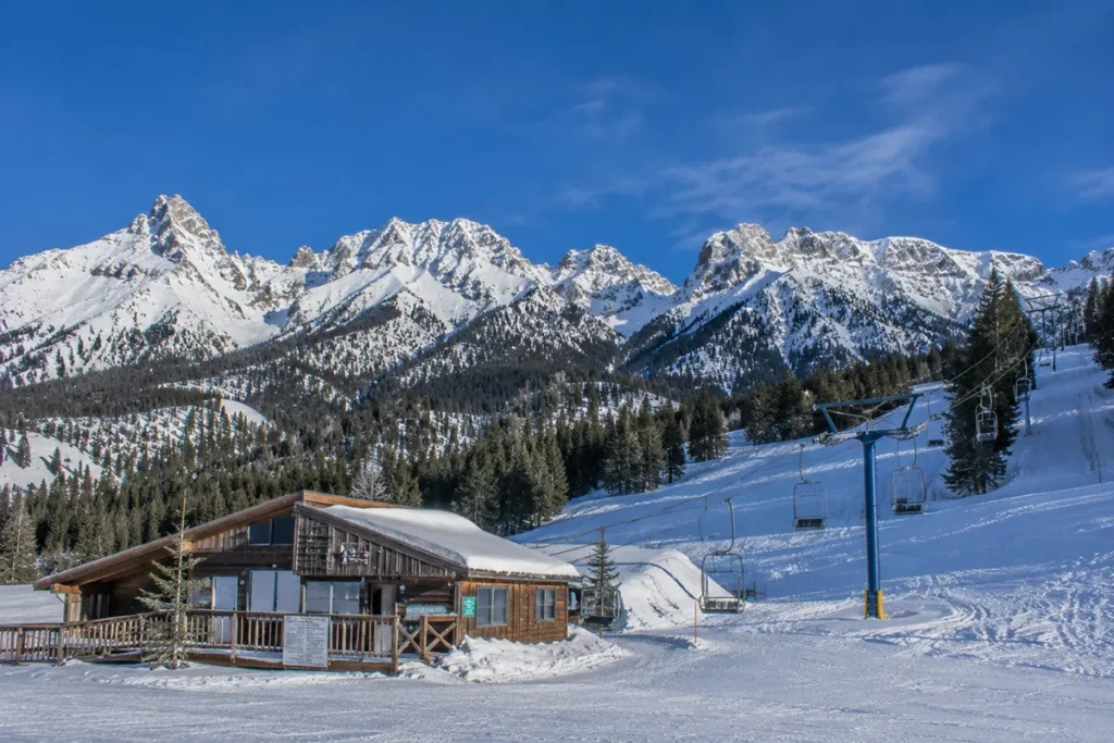 View of the small base lodge and single double chairlift at Maverick Mountain Ski Area with snow-capped Pioneer Mountains rising in the background under a clear winter sky