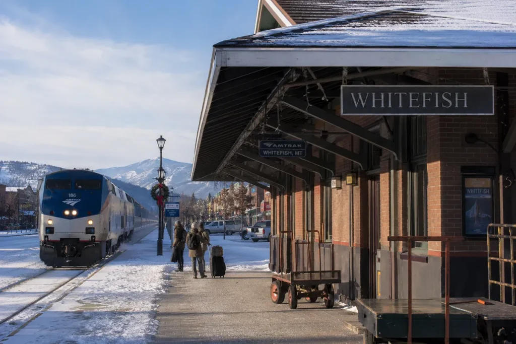 The historic Amtrak Whitefish train station with the Empire Builder train arriving on a snowy winter morning and historic buildings of downtown Whitefish visible