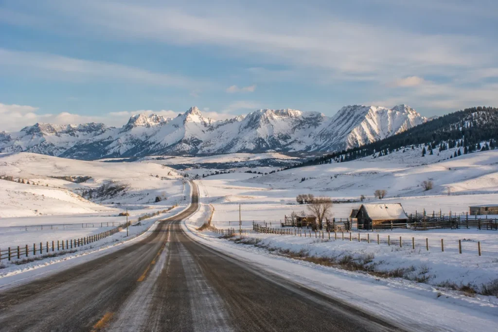 Snow-covered road approaching Maverick Mountain through ranchland and rolling foothills with the Pioneer Mountains rising in the distance