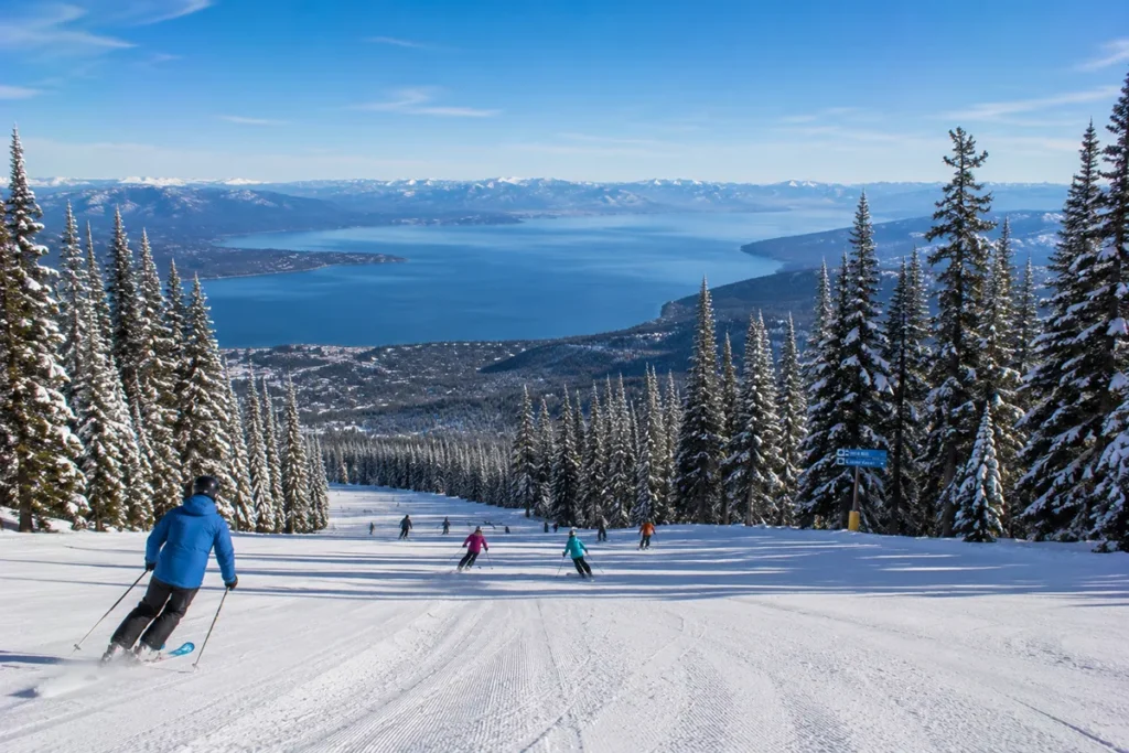 Multiple skiers descending a wide groomed intermediate run at Blacktail Mountain with Flathead Lake visible far below in the valley