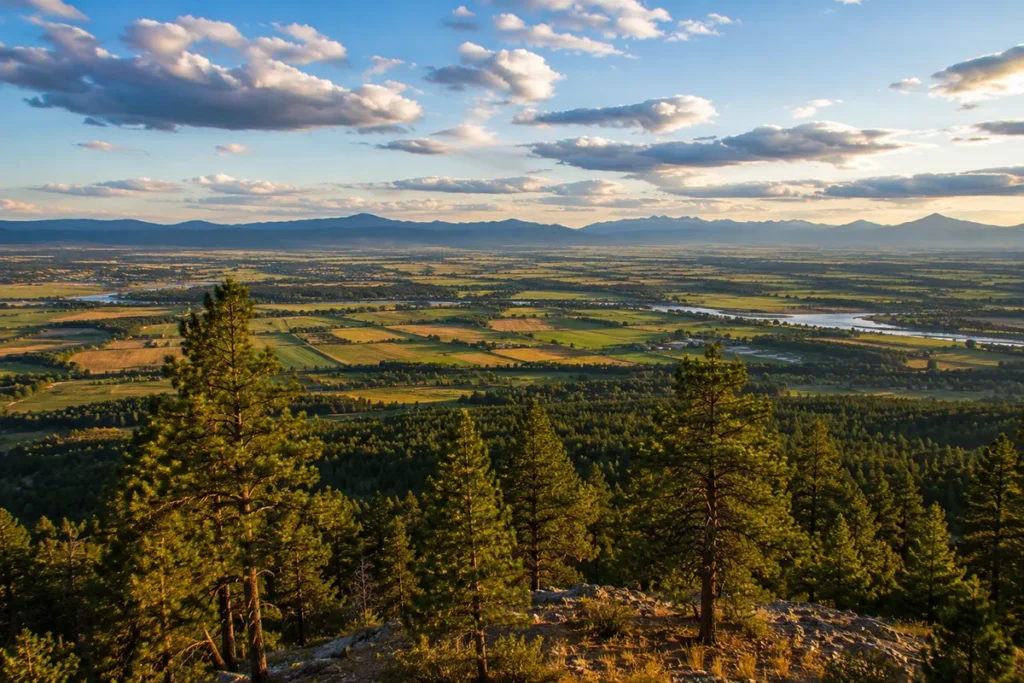 Panoramic view from Lone Pine State Park overlook showing the Flathead Valley below, with the Mission Mountains and Glacier National Park peaks in the distance