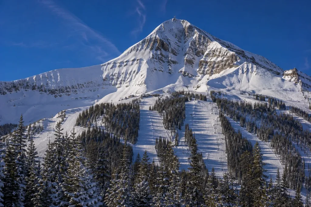 Lone Peak rising dramatically above the snow-covered slopes of Big Sky Resort in Montana on a clear bluebird day with the Lone Peak Tram cable visible going up to the summit