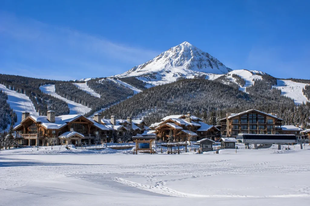 Wide view of the Moonlight Basin base area at Big Sky Resort with private lodging and the original Moonlight Lodge visible against the backdrop of the north face of Lone Mountain