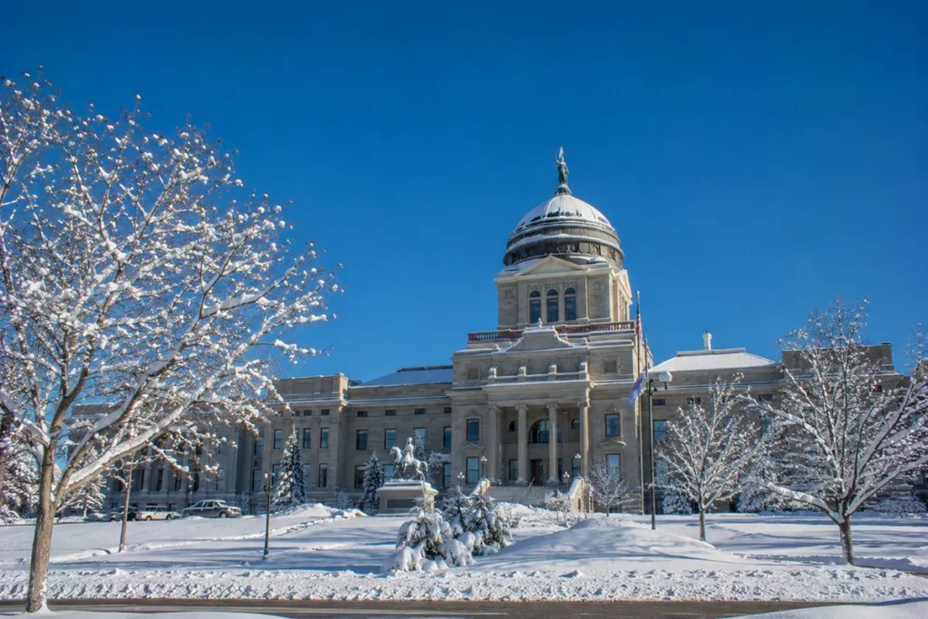 The Montana State Capitol building in Helena with snow on the dome and grounds visible on a sunny winter day