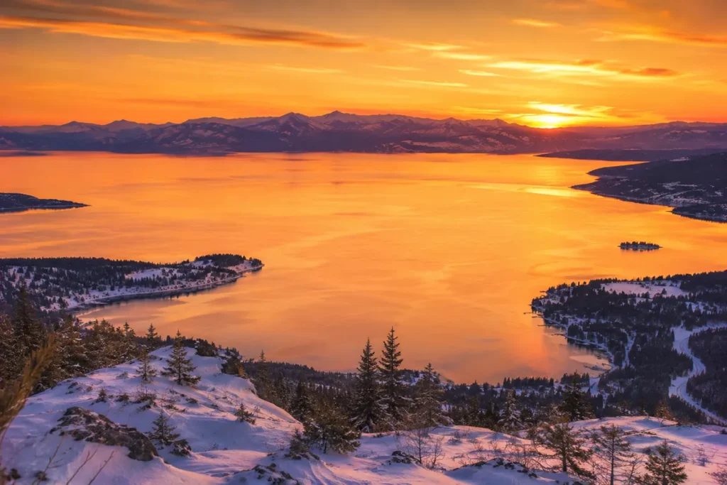 Alpenglow on Flathead Lake at sunset with the lake surface lit up in golden orange tones and snow-covered shores visible