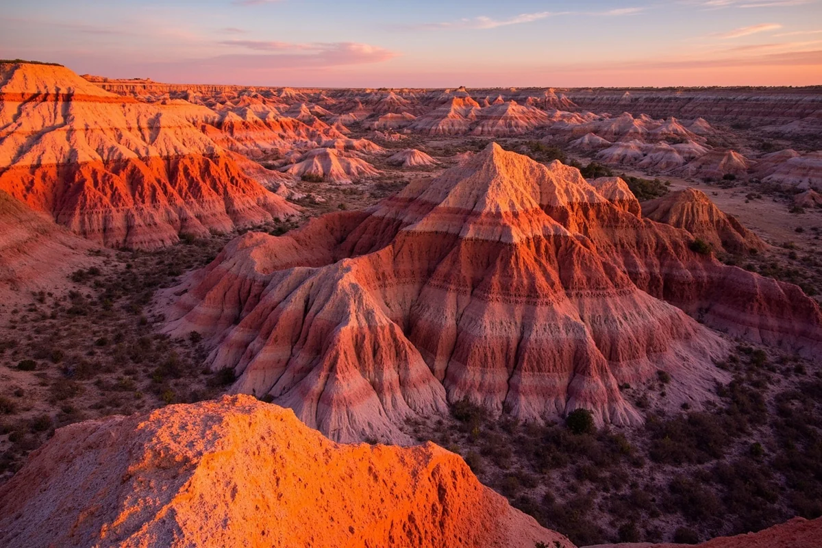 Colorful badland formations in the Terry Badlands Wilderness Study Area at golden hour, with warm orange and red lighting on the rock layers