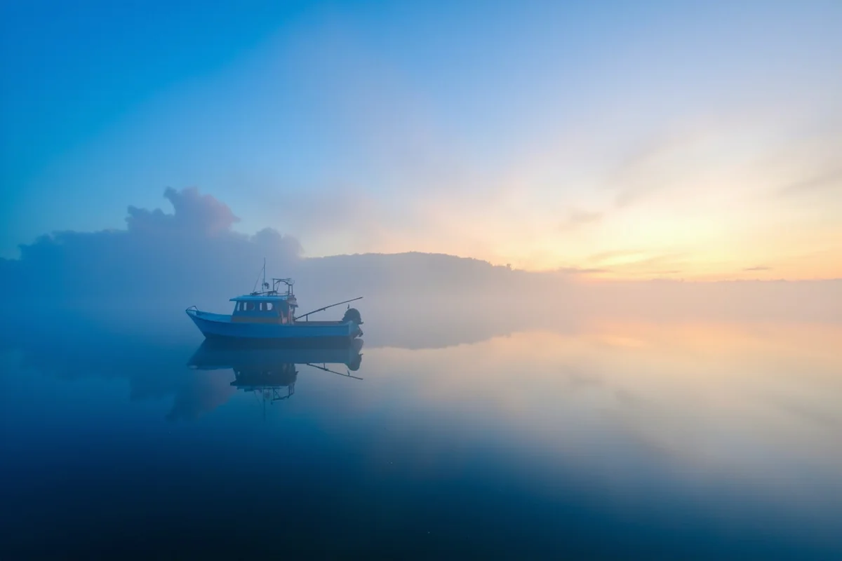 Fishing boat at dawn on Lake Elwell with fog over the water and blue sky reflecting on the surface
