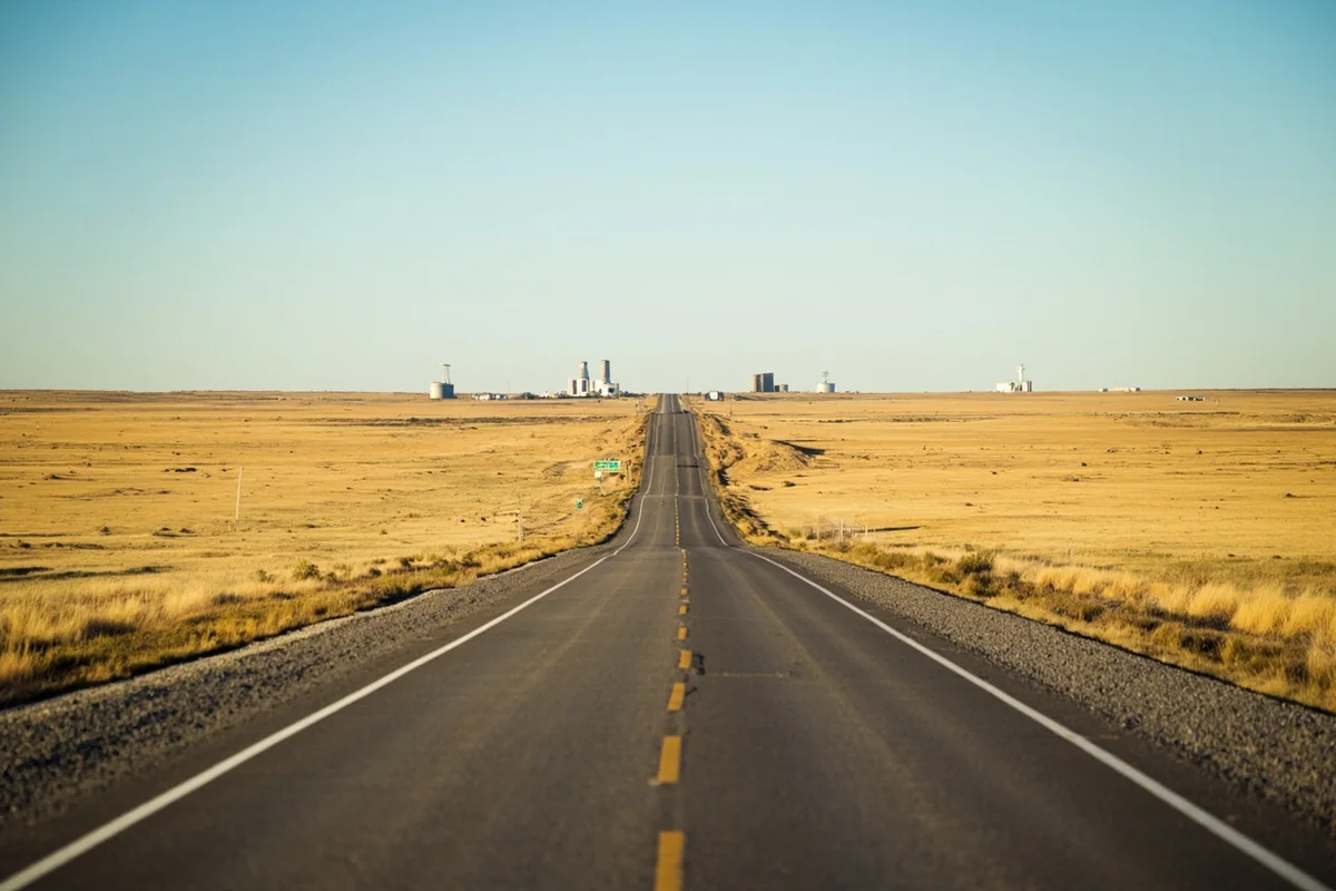 US Highway 2 cutting through open Hi-Line prairie near Havre with grain elevators visible in the distance