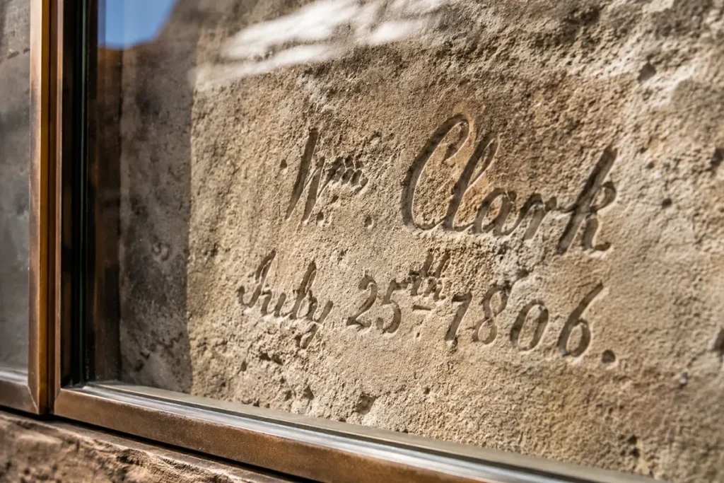 Close-up of William Clark's 1806 signature carved into sandstone rock at Pompeys Pillar, protected behind glass