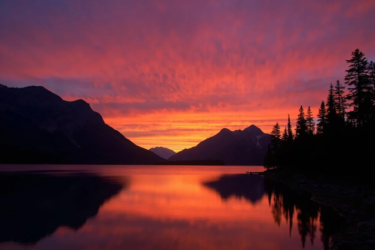 Sunset light over Bowman Lake with mountains silhouetted against an orange sky